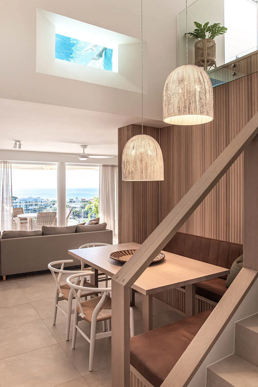 Dining area with woven pendant lights and ocean views beyond the living room